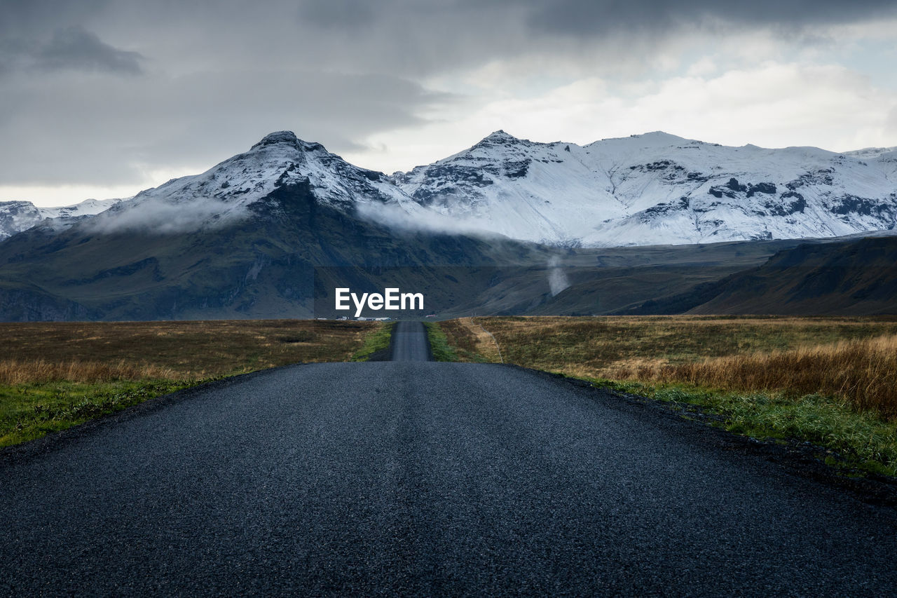 Road towards the scenic snow covered mountains  in the rural countryside of south iceland