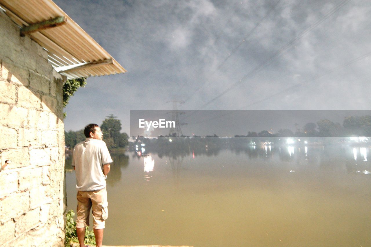 FULL LENGTH OF MAN STANDING BY WATER AGAINST SKY