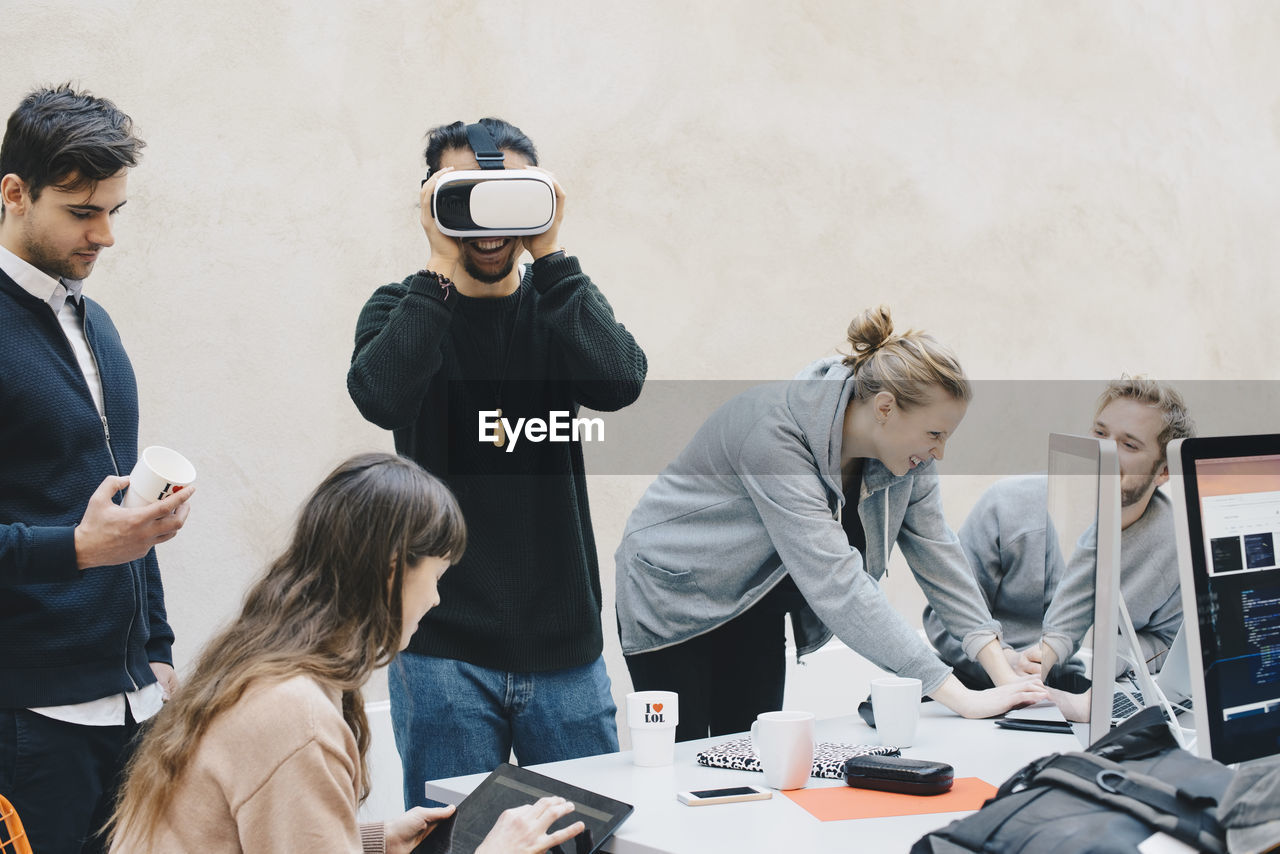 Male computer programmer using vr glasses while colleagues working in office