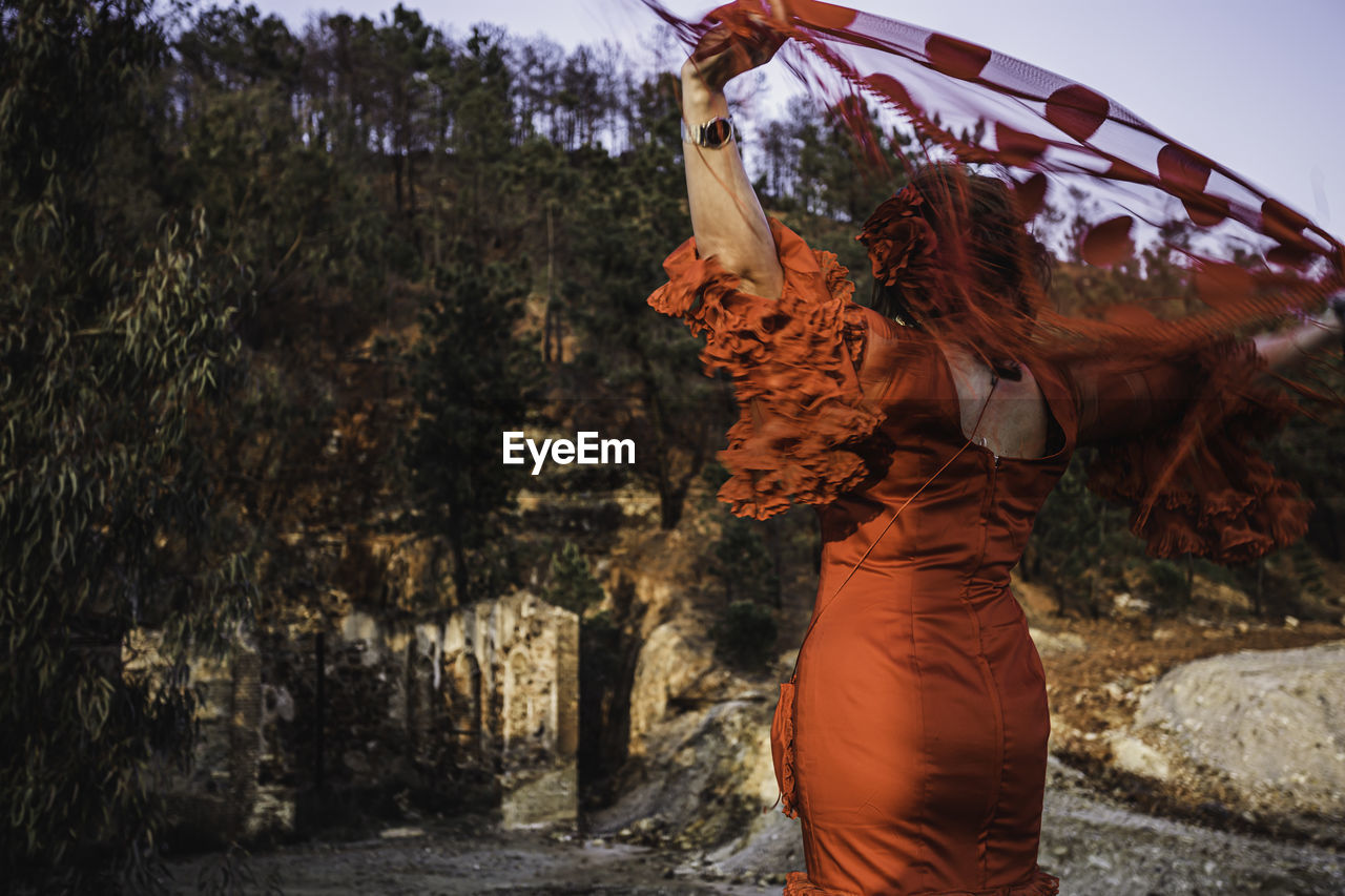 Rear view of woman holding fabric while standing against trees