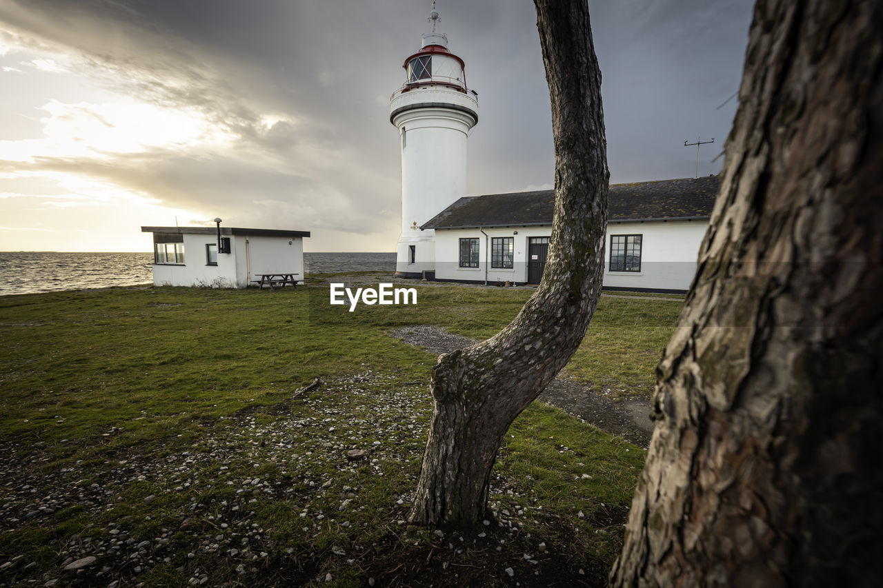 LIGHTHOUSE AMIDST BUILDINGS AGAINST SKY