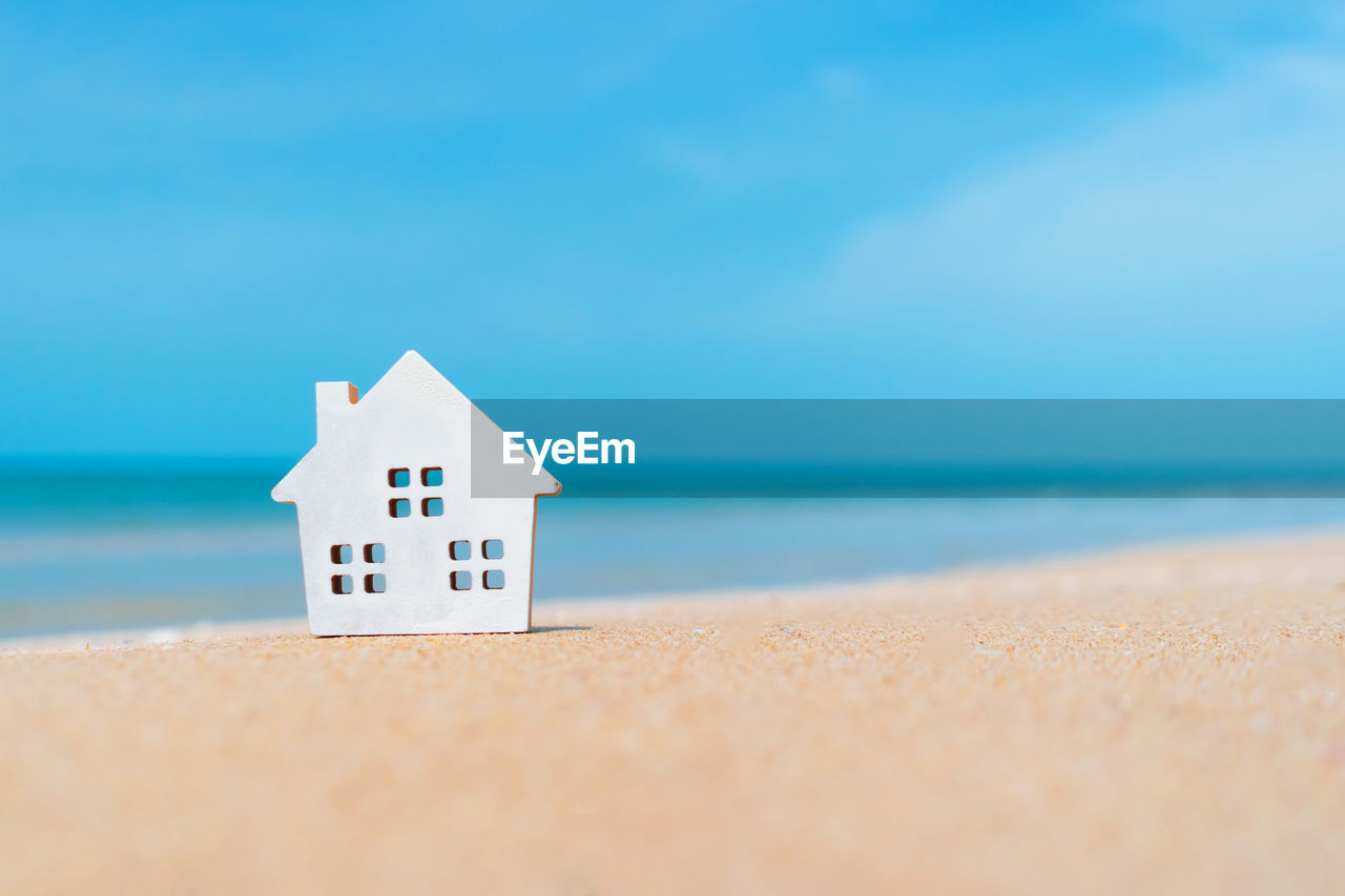 Closed up tiny home models on sand with sunlight and beach background.