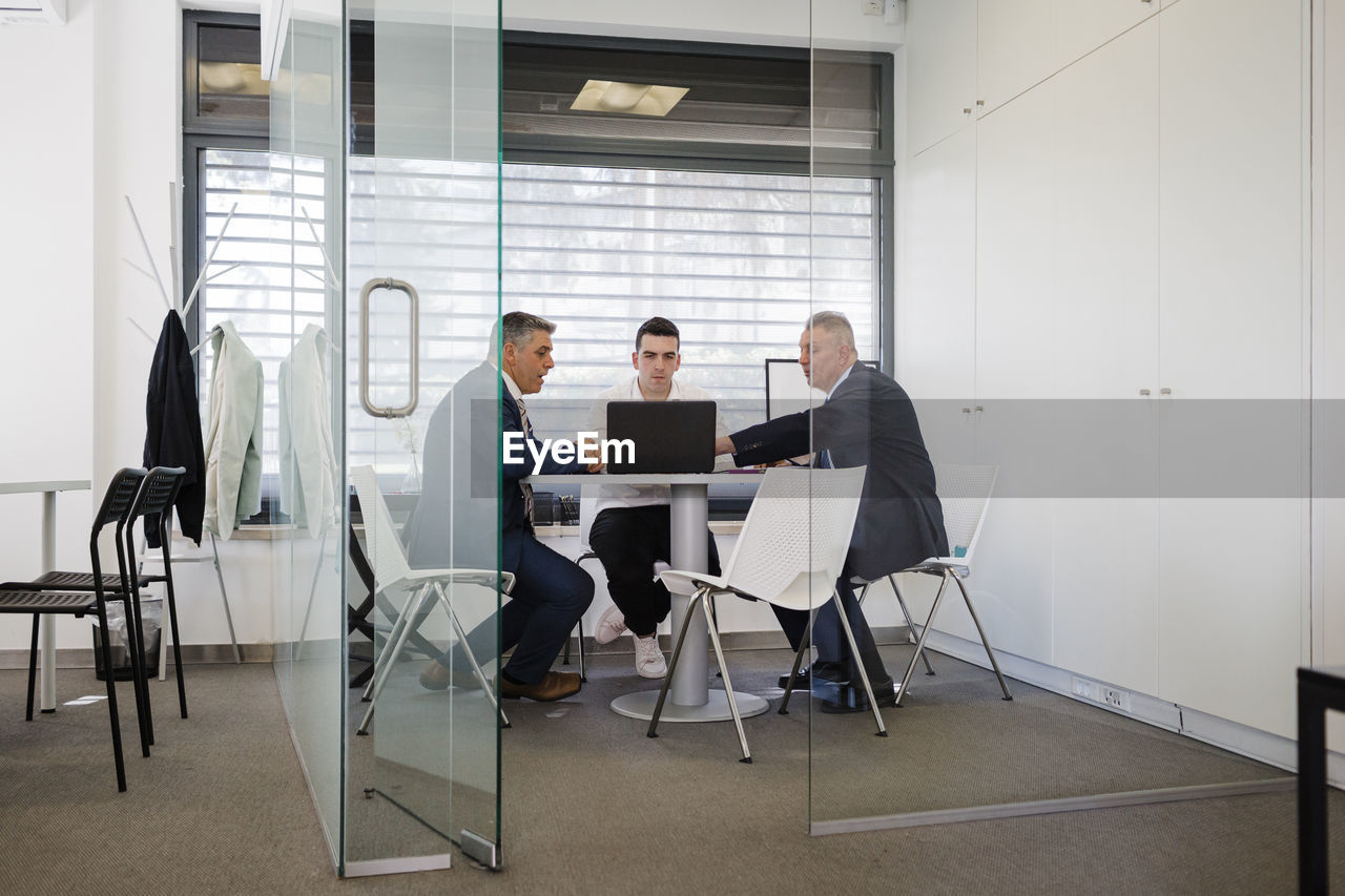 Mature businessman discussing over laptop with colleagues sitting at desk in office