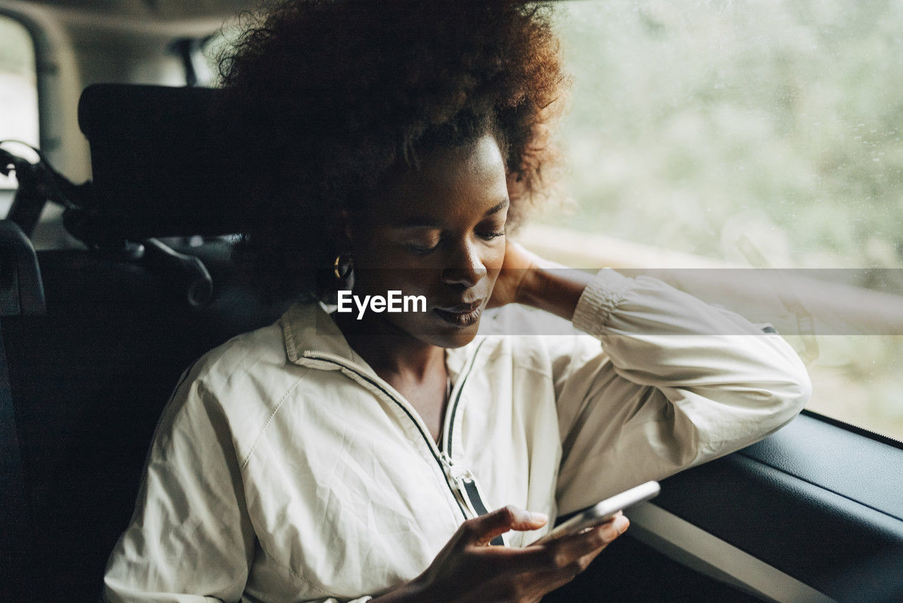 Young afro woman using smart phone while sitting in van during road trip