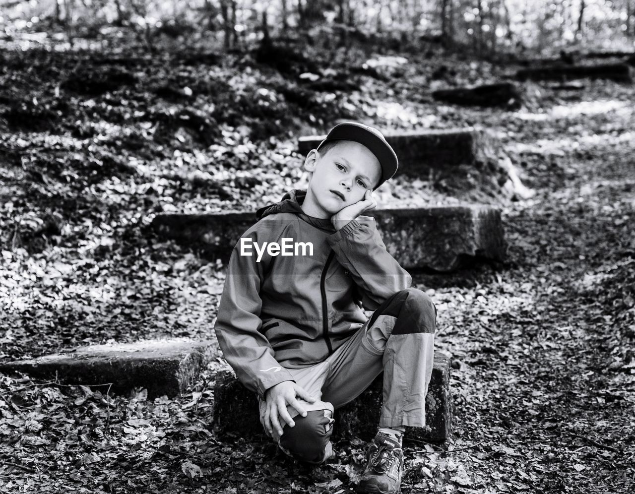 Portrait of cute boy sitting on field in forest