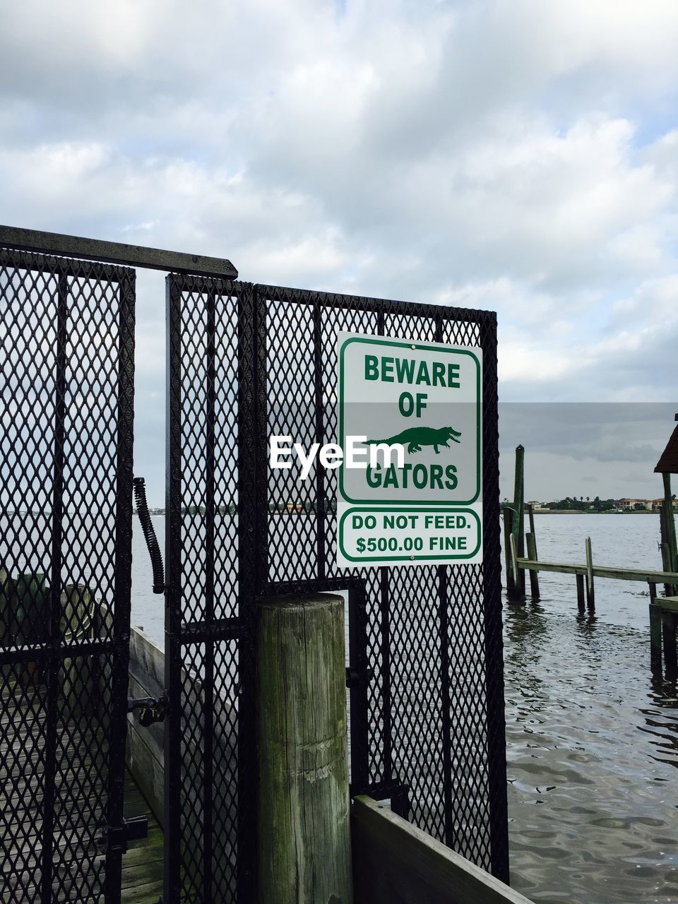 Warning sign on metal grate by sea against cloudy sky