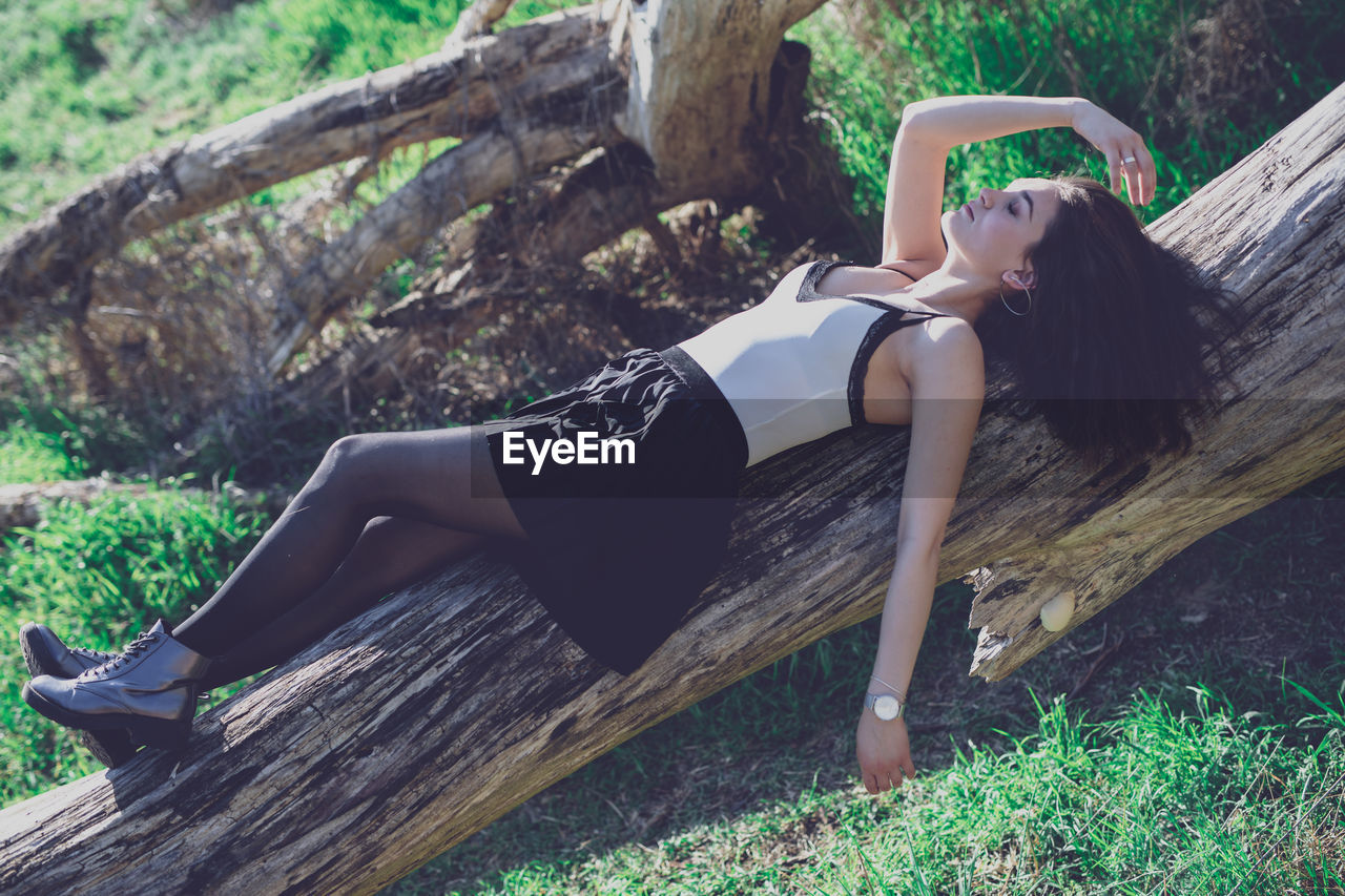 YOUNG WOMAN LYING ON TREE TRUNK