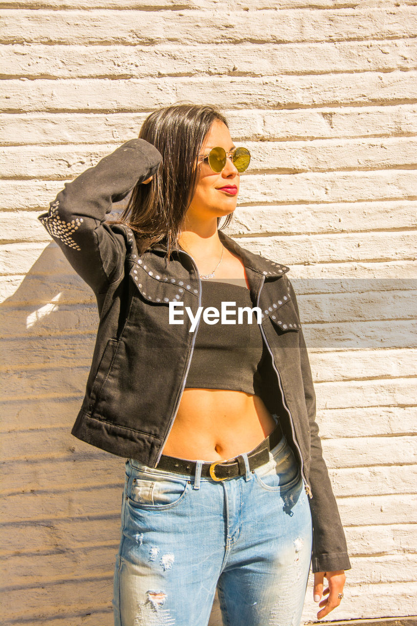 Young woman wearing sunglasses standing against wall