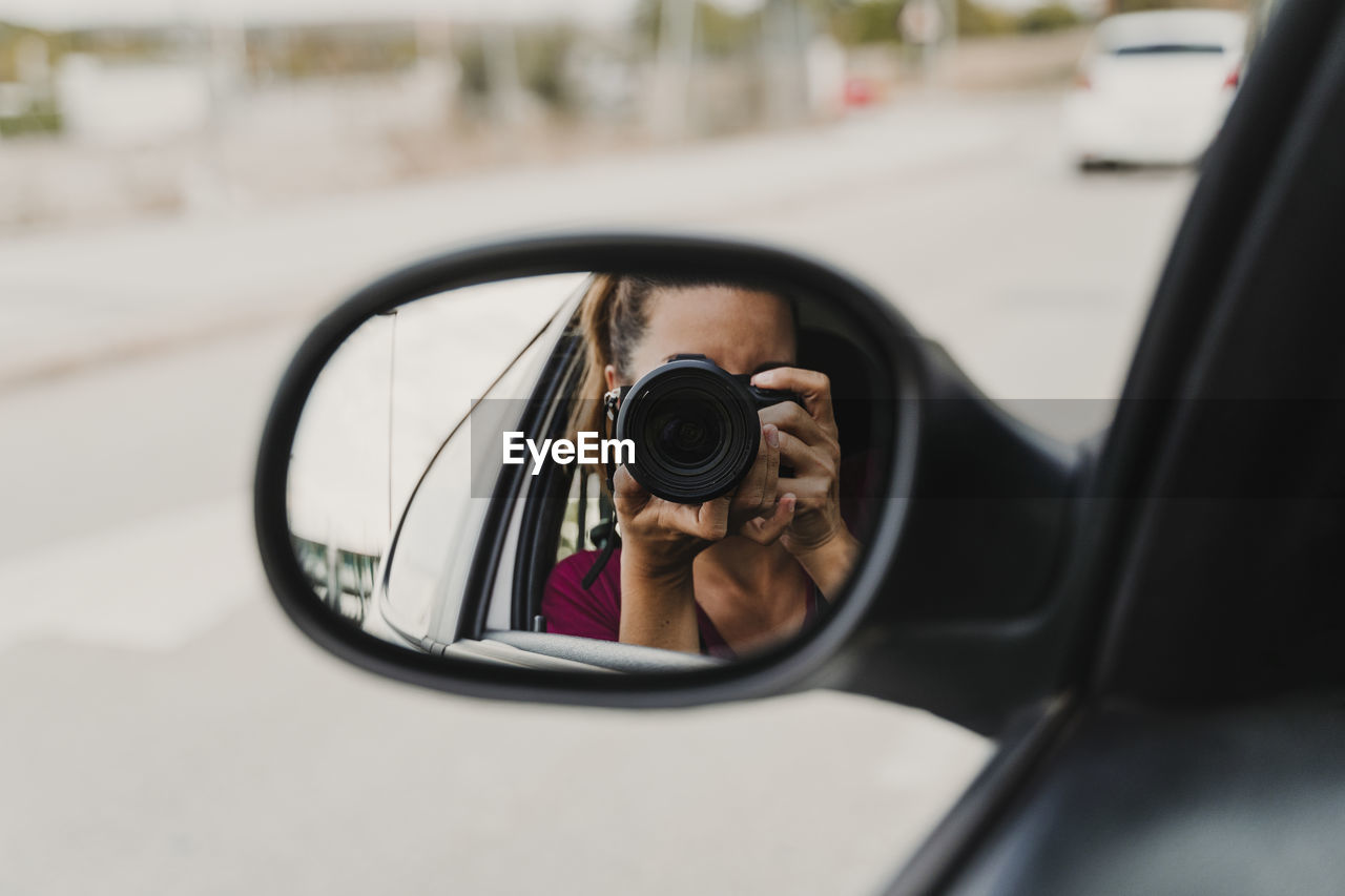 Woman photographing reflecting on side-view mirror