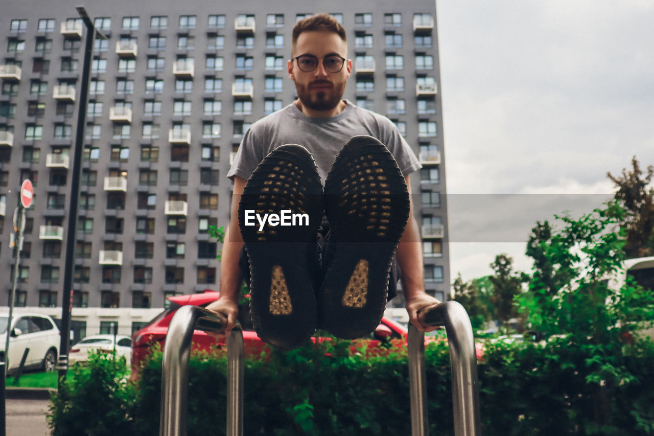 Portrait of young man sitting against buildings in city