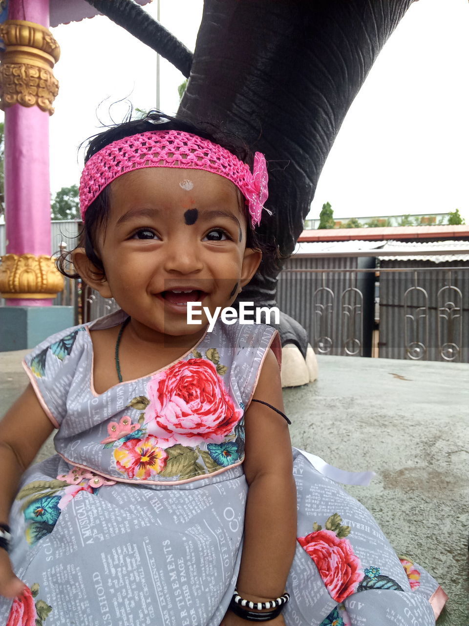 childhood, child, one person, portrait, toddler, looking at camera, women, smiling, clothing, female, happiness, front view, person, cute, emotion, day, baby, lifestyles, innocence, architecture, fashion accessory, sitting, three quarter length, casual clothing, hat, outdoors, leisure activity, nature, cheerful, traditional clothing, human face, built structure