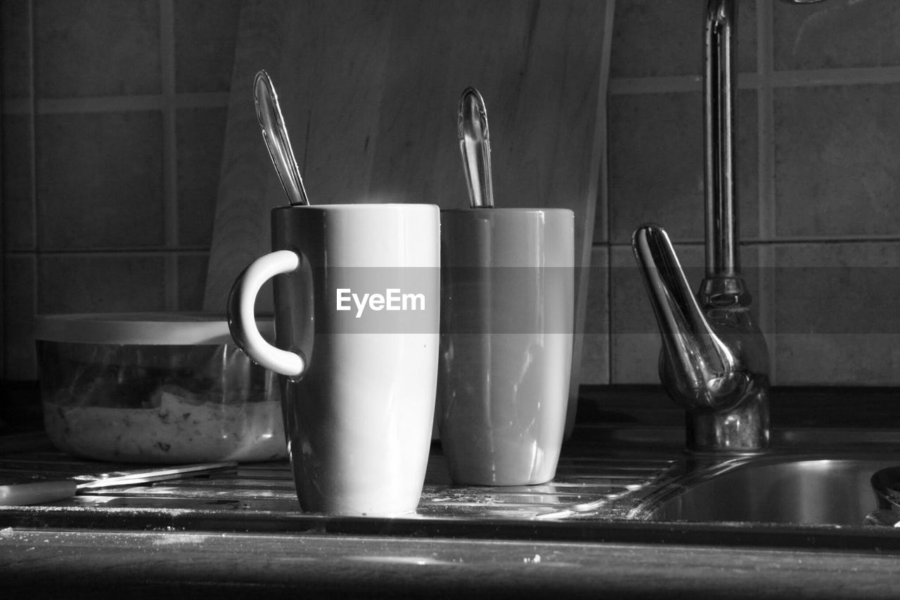 Close-up of mugs by kitchen sink