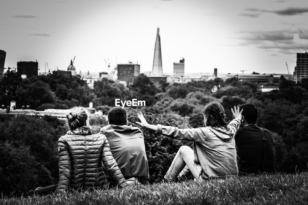 Rear view of friends sitting on grass in park against sky