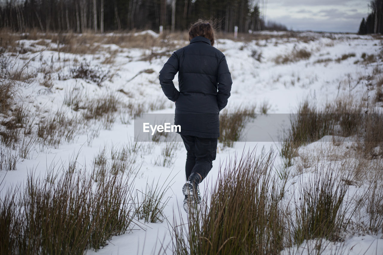 REAR VIEW OF MAN STANDING ON SNOW FIELD