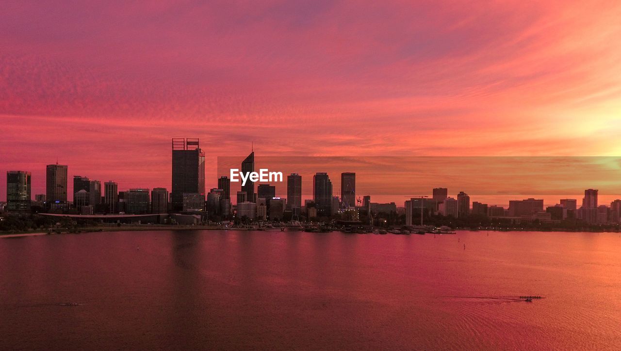 Sea and buildings against sky during sunset