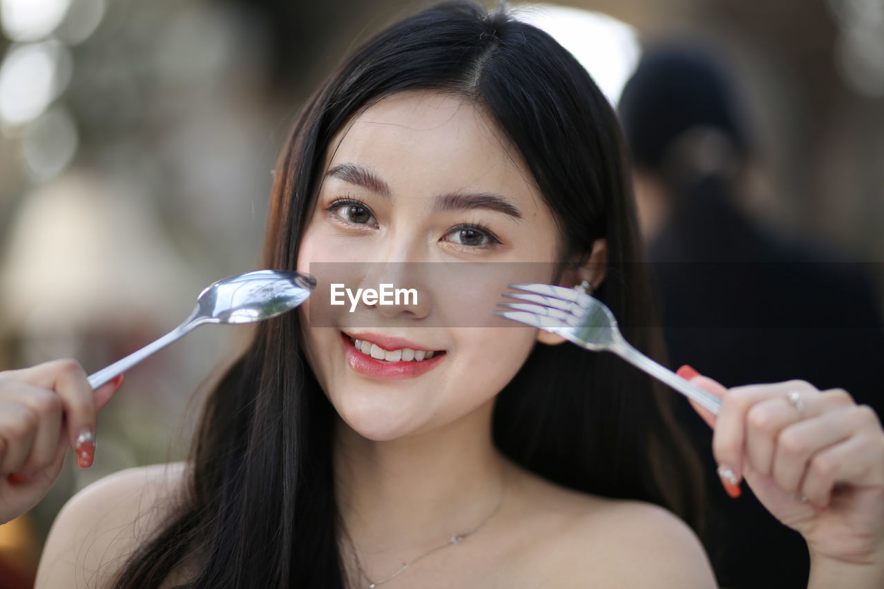 Close-up portrait of smiling woman holding spoon and fork