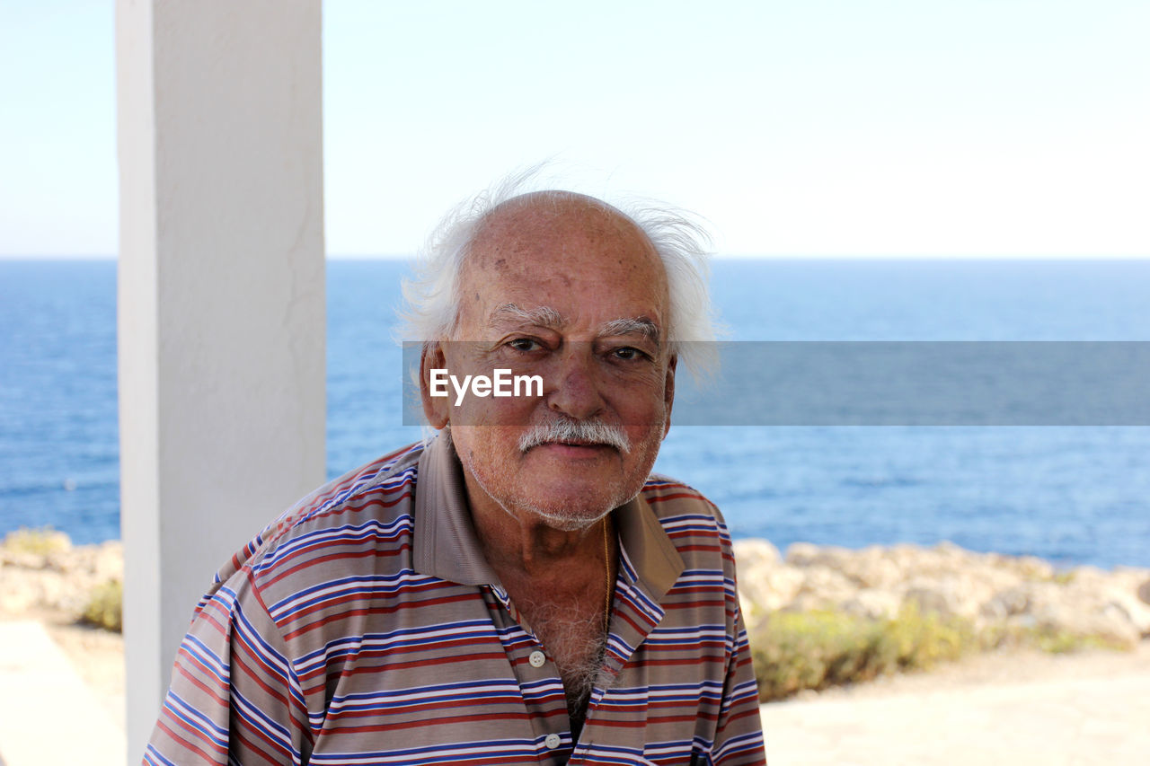 PORTRAIT OF MAN STANDING AT BEACH AGAINST SKY