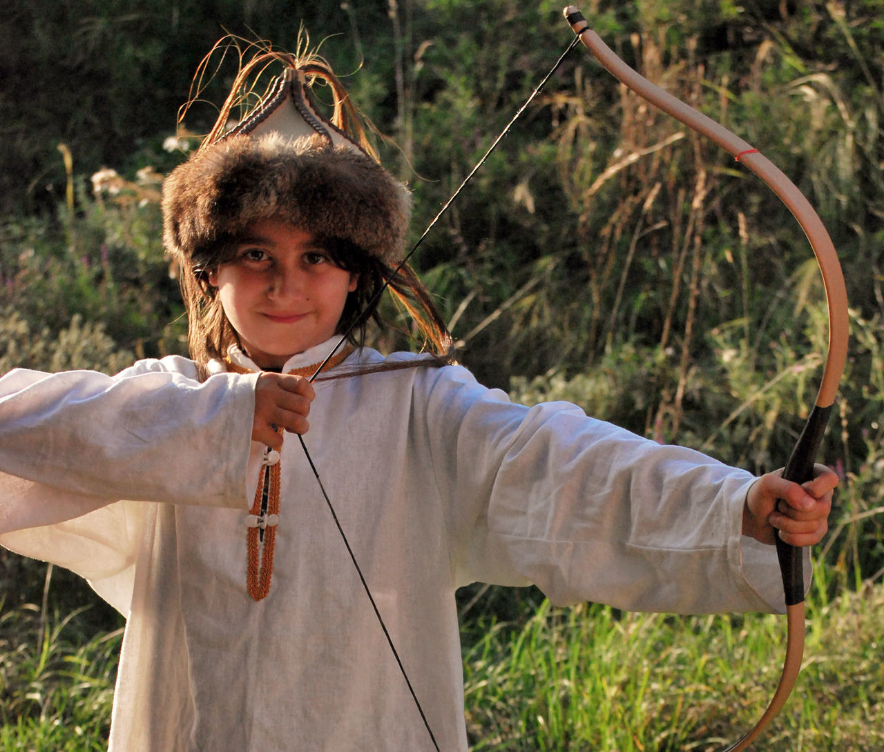 Portrait of smiling girl stretching bow while standing on field