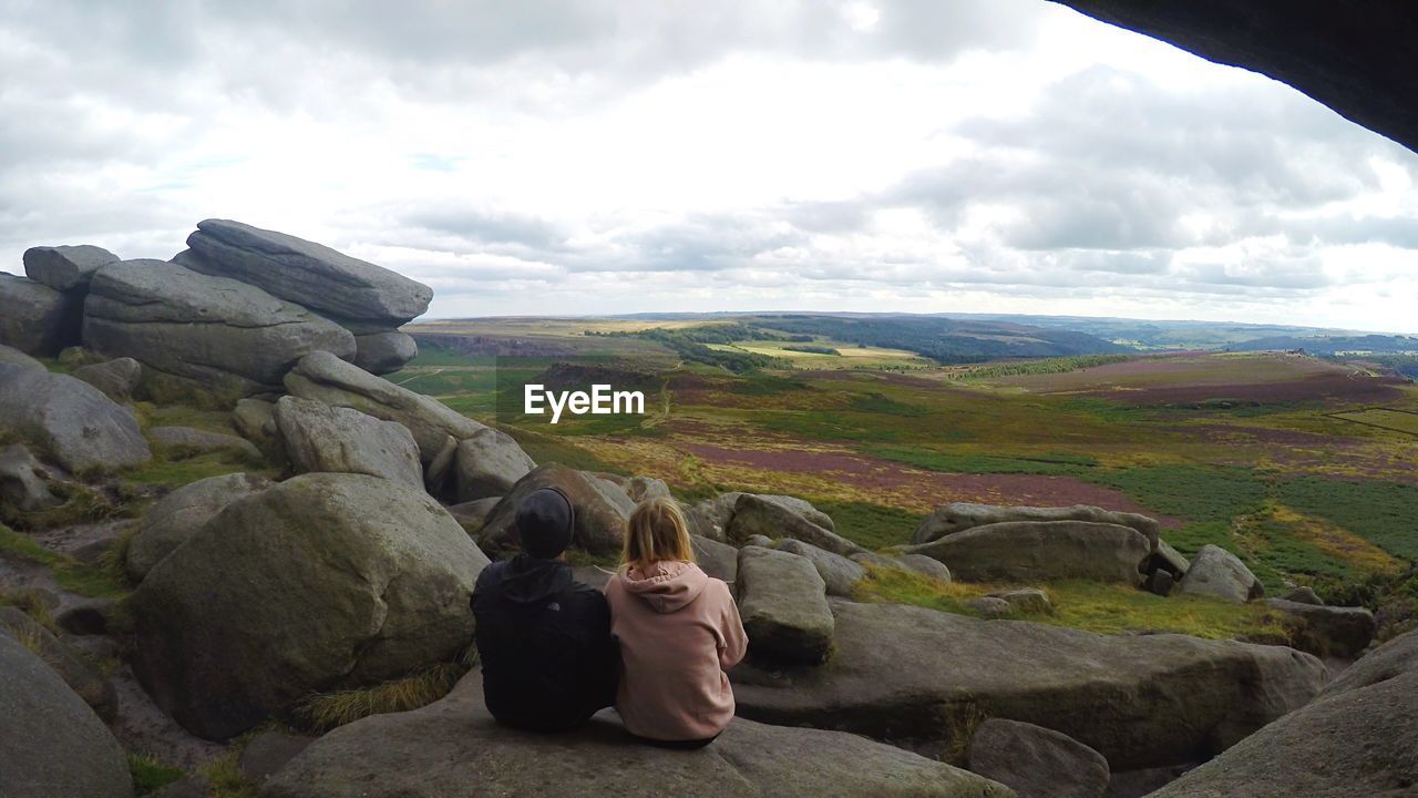 real people, sky, one person, nature, leisure activity, rear view, cloud - sky, lifestyles, beauty in nature, day, sitting, outdoors, mountain, standing, casual clothing, tranquil scene, women, rock - object, tranquility, scenics, full length, landscape, men, people