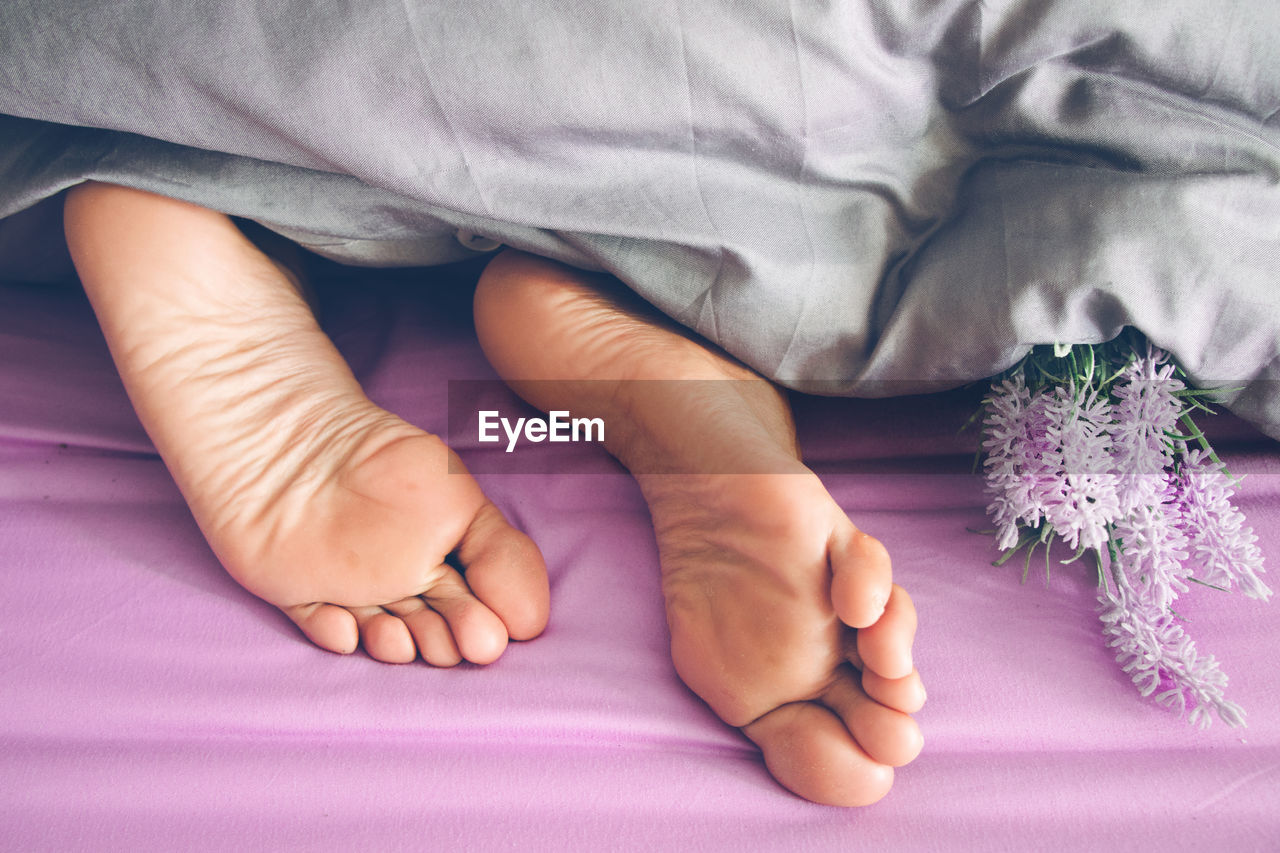 Low section of man by flower lying under blanket on bed