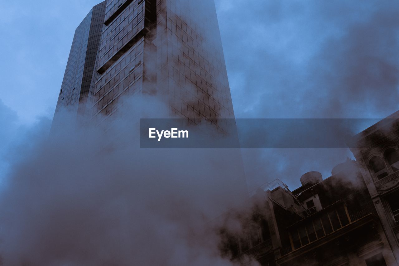 Low angle view of modern buildings and smoke in city against sky