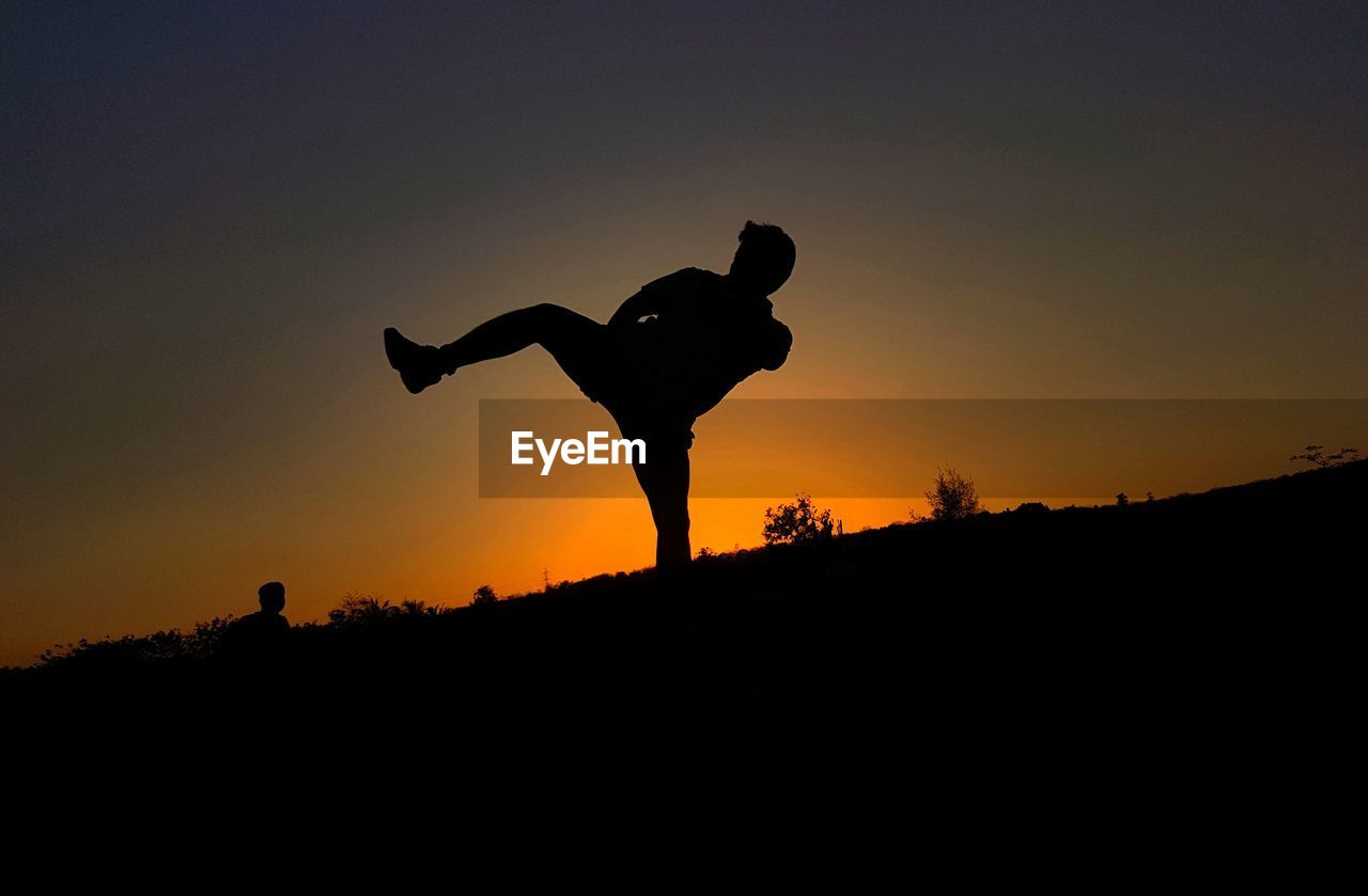 Silhouette of man kickboxing at field against sky during sunset