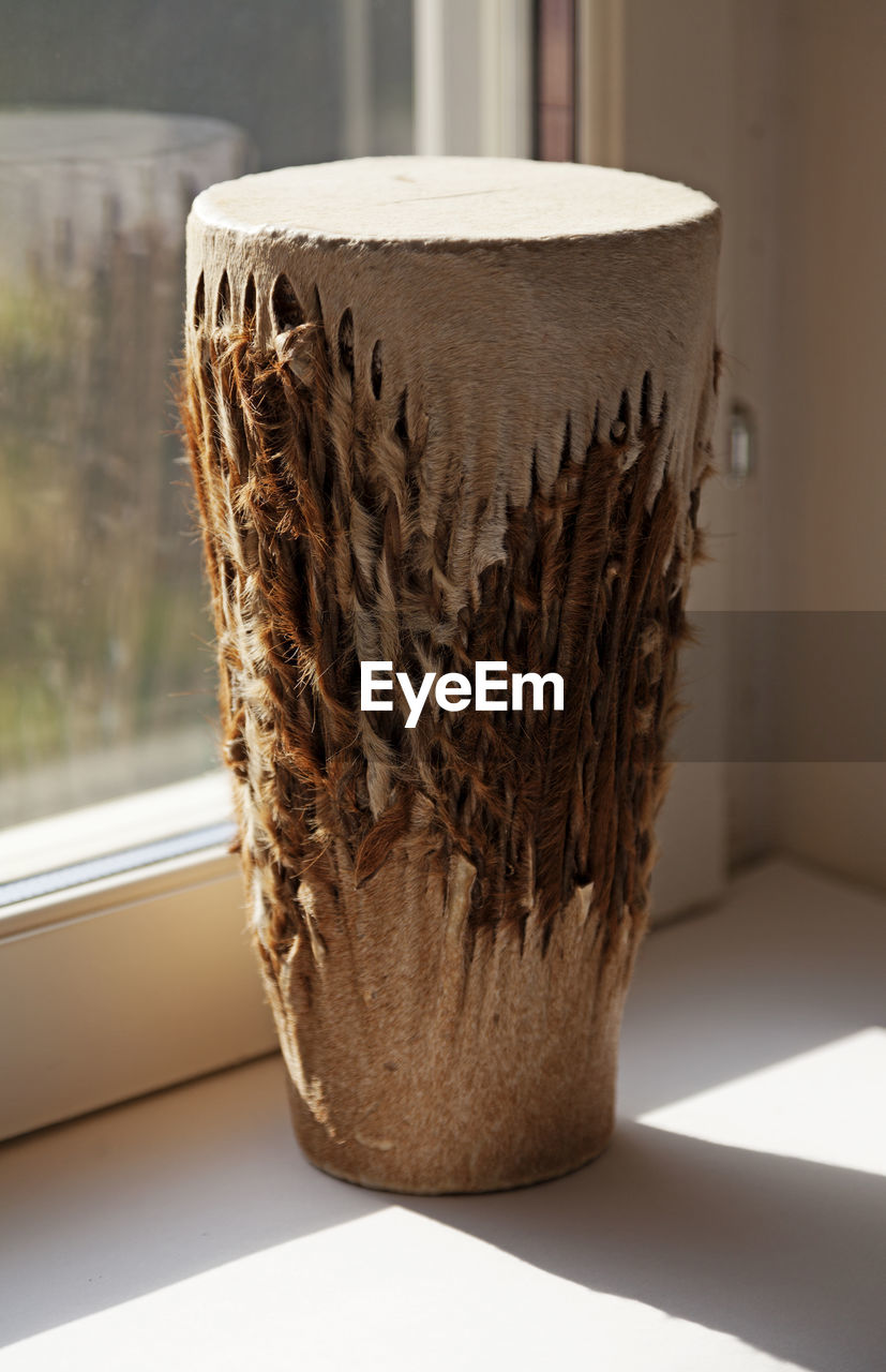 A tall traditional drum standing in the windowsill with sunlight