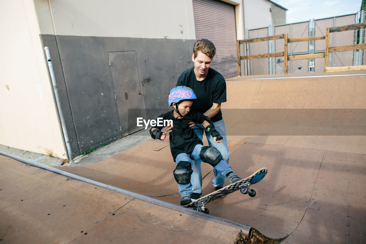 Skateboarding instructor holds boy helping him turn on half pipe