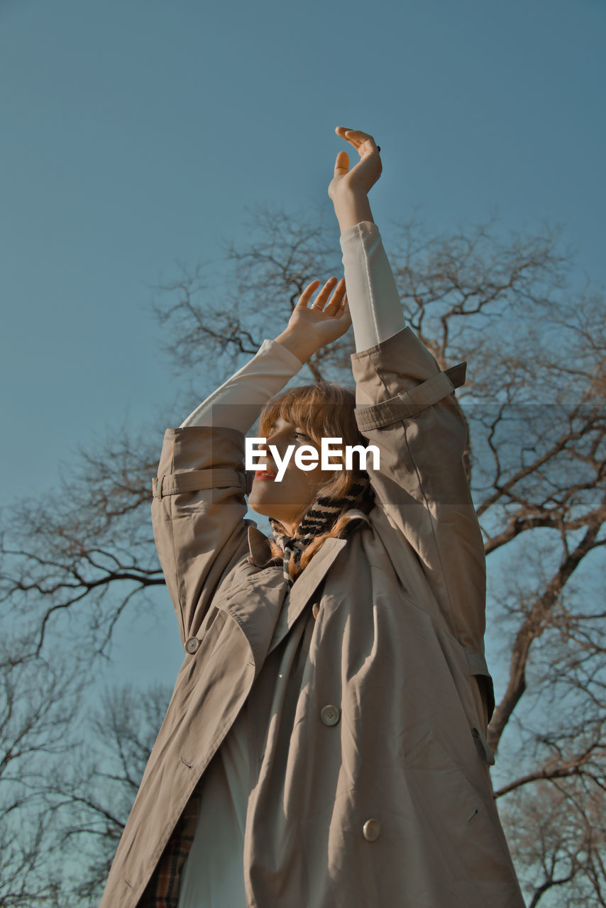 Low angle view of woman standing by bare tree against sky