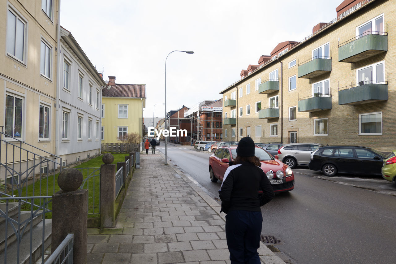 REAR VIEW OF PEOPLE WALKING ON ROAD AMIDST BUILDINGS IN CITY