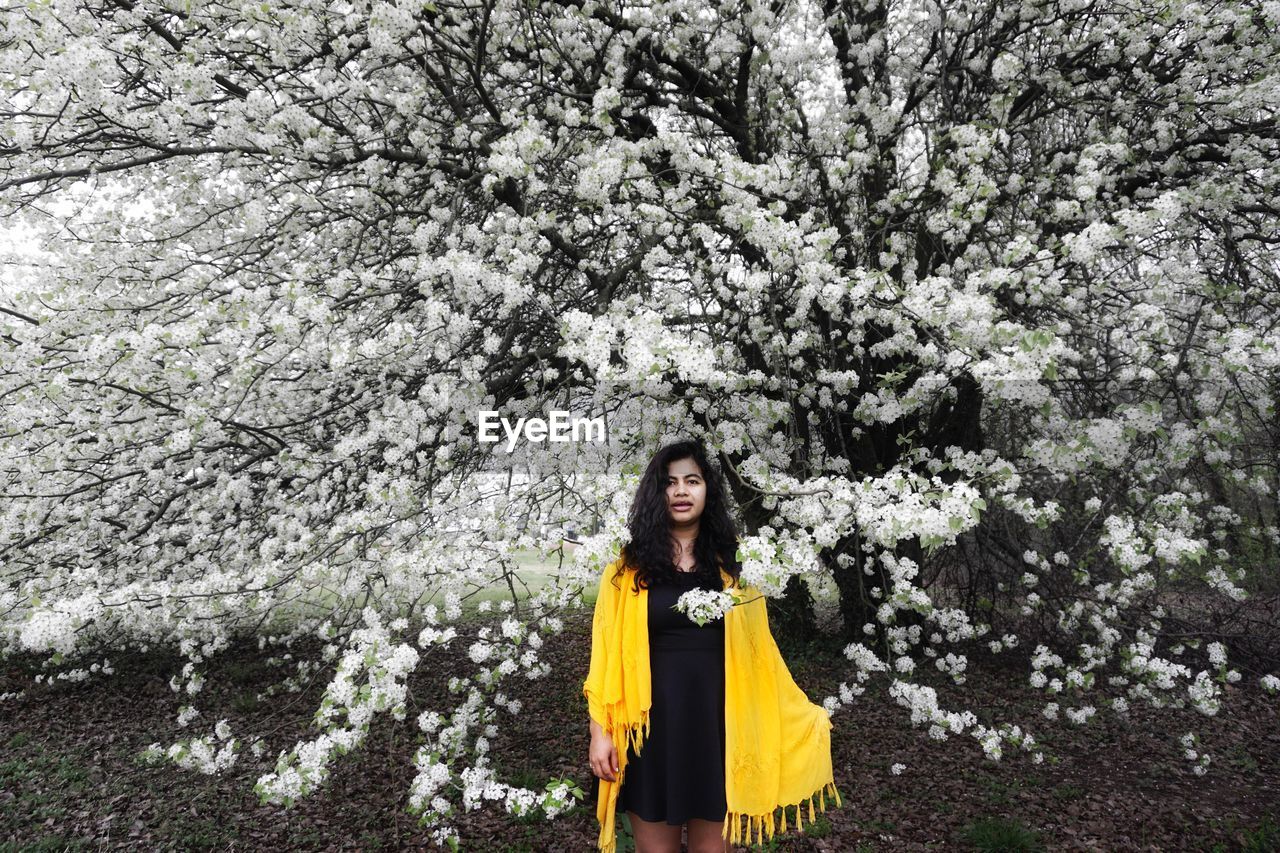 Portrait of young woman standing by flowering tree