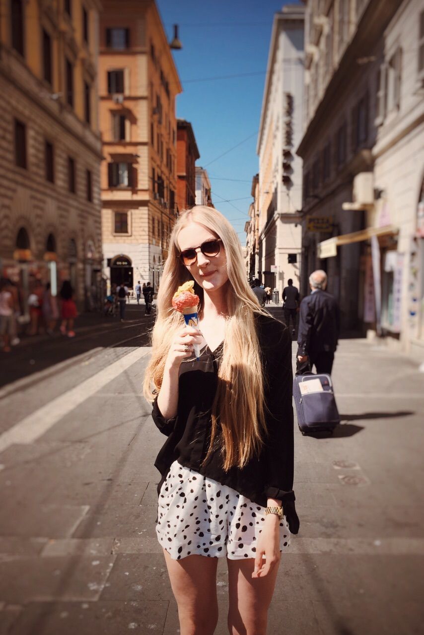 Young woman holding ice cream on street amidst buildings