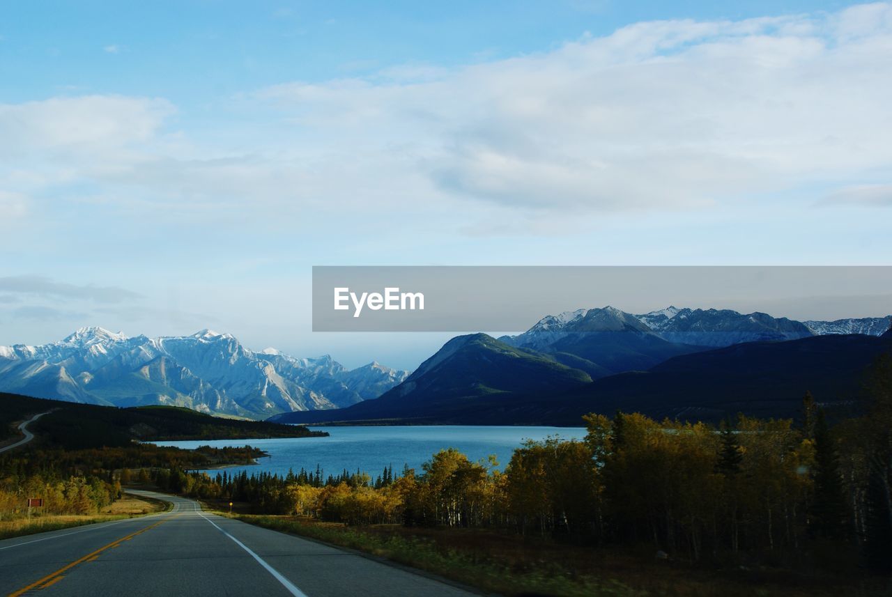 Country road by lake and mountains against sky