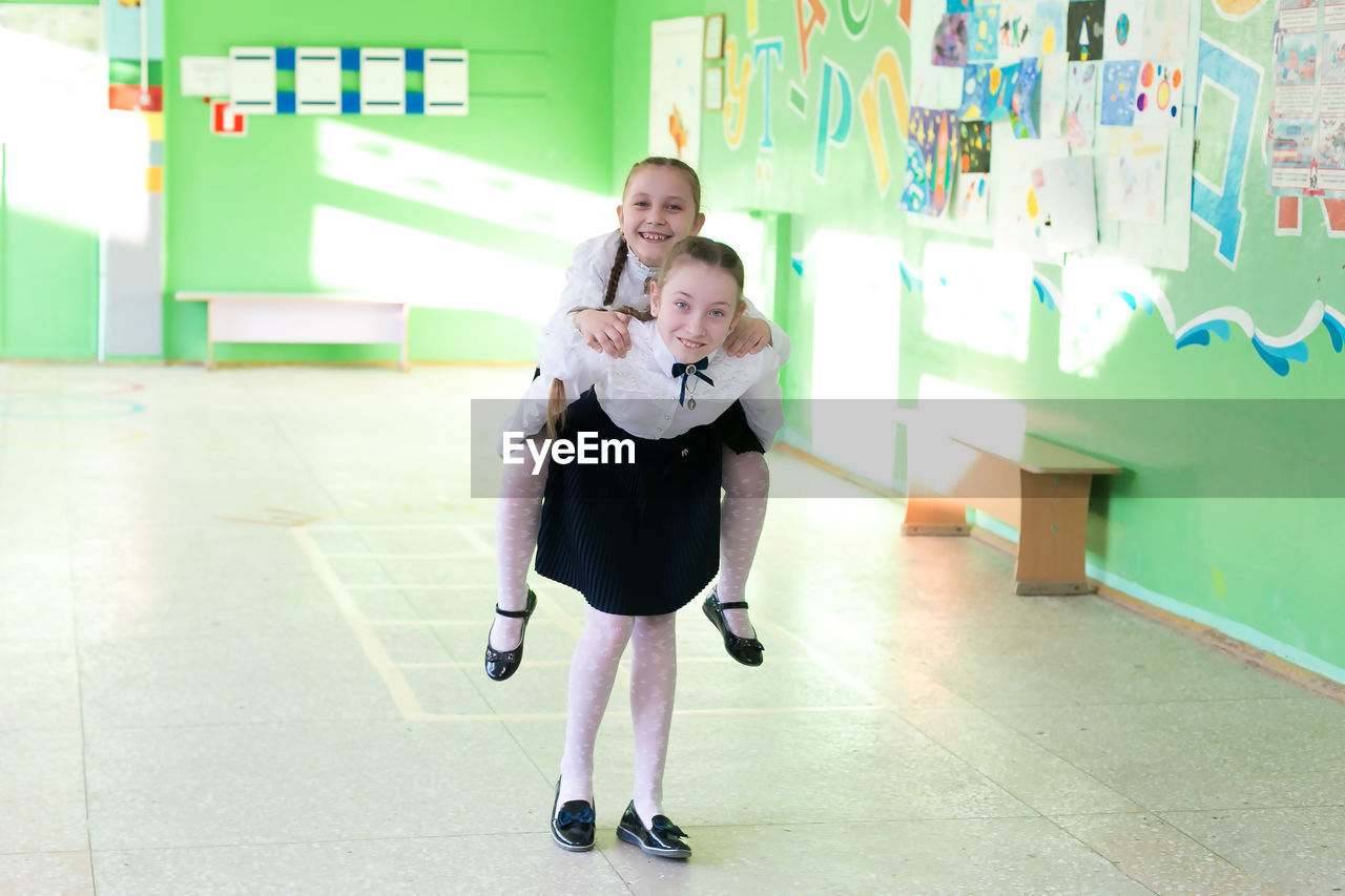 Full length of girl carrying friend on back at school