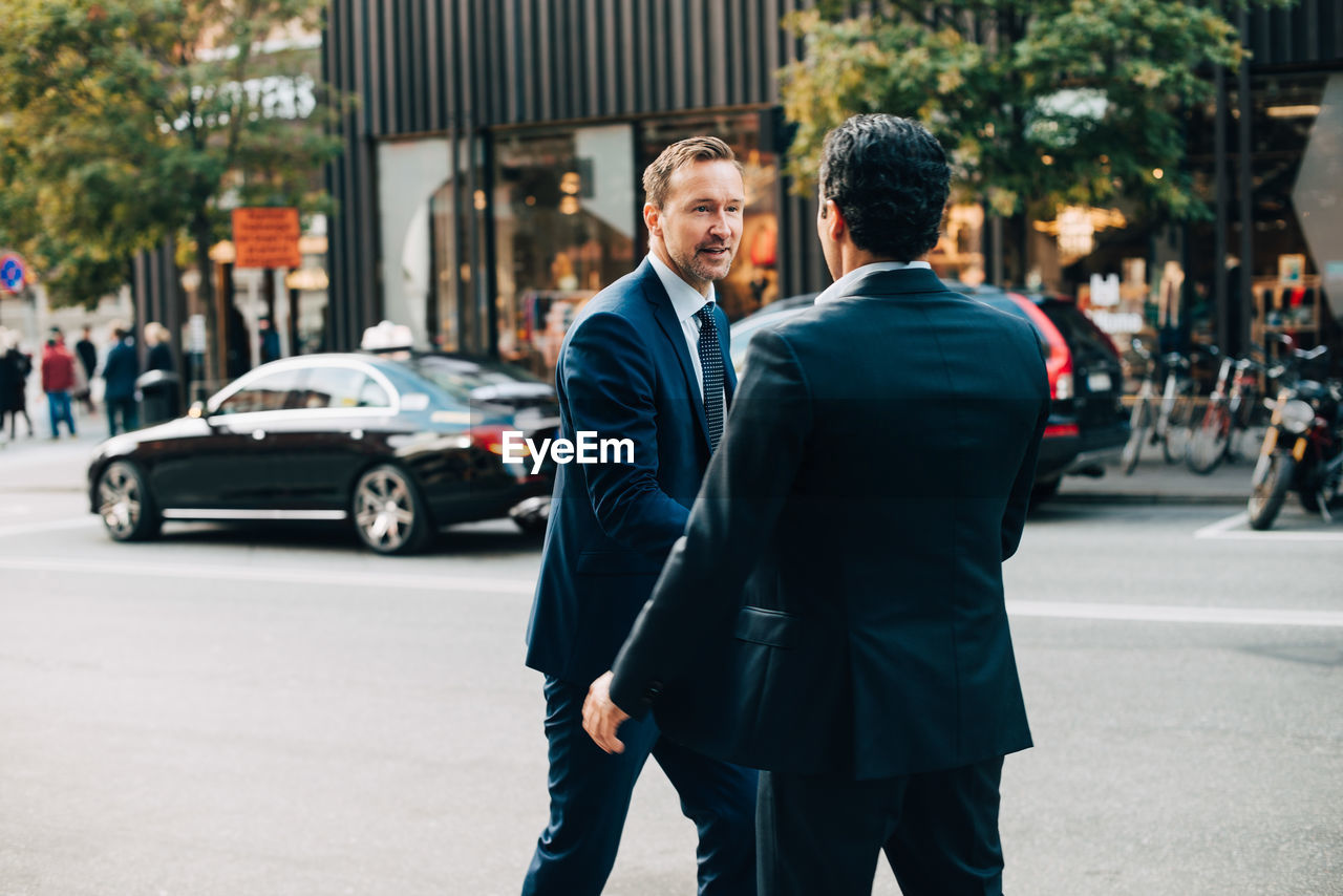 Mature businessman greeting male colleague on street in city