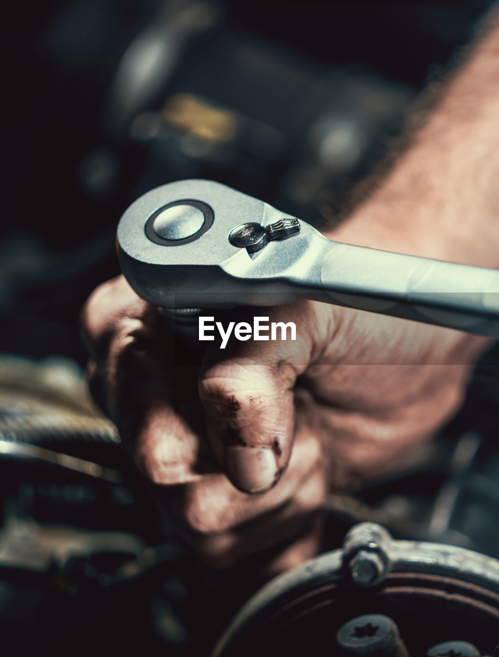 Cropped hands of mechanic repairing engine of car