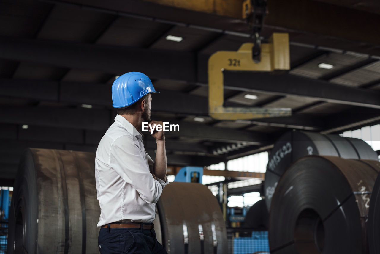 Businessman with hand on chin standing in factory