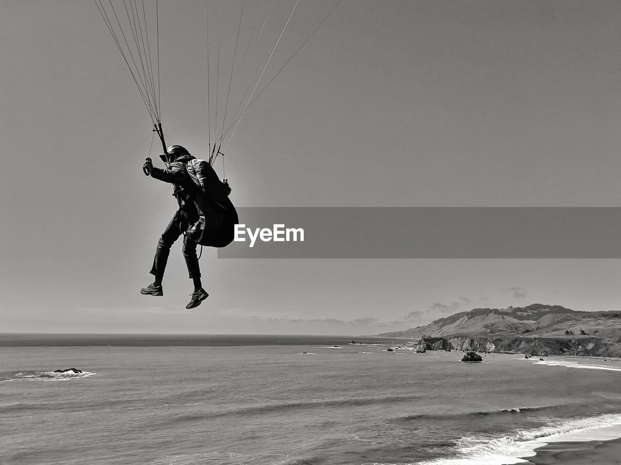 Man paragliding over the ocean against cliffs.