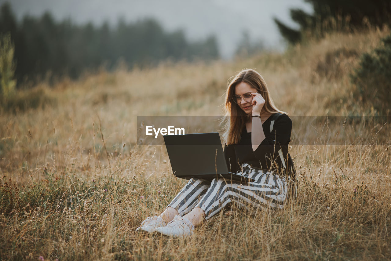 Happy woman freelancer with glasses working on laptop, remote location in nature