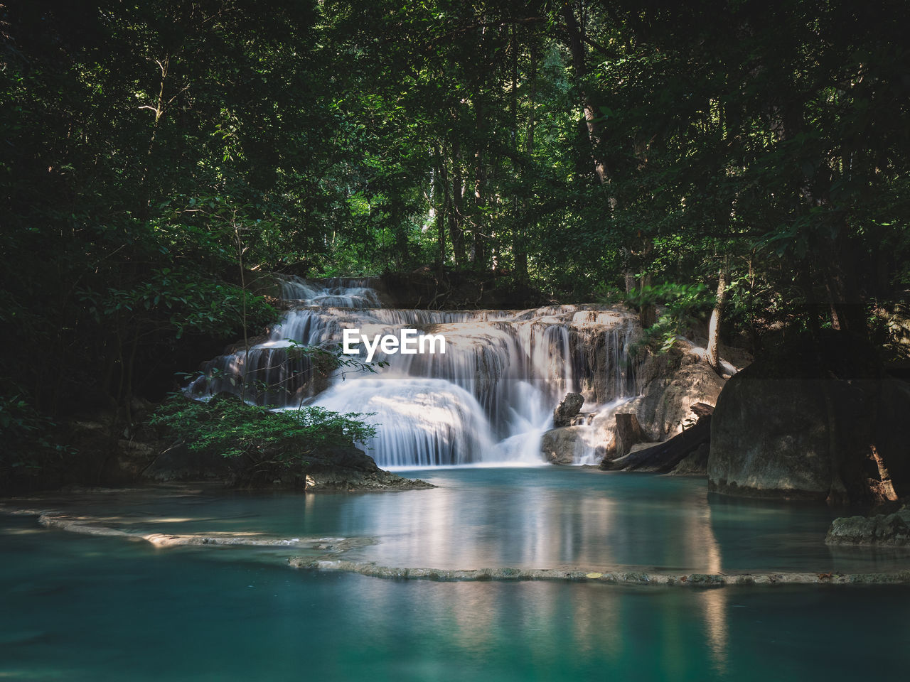 Waterfall smooth flowing stream with emerald pond and sunlight in rainforest. erawan falls, thailand