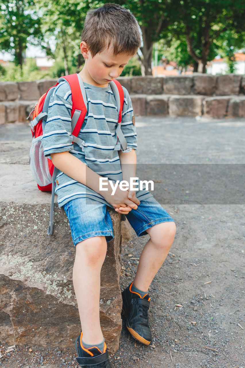 A sad schoolboy sits in the school yard with a backpack on his back. children's problems at school.