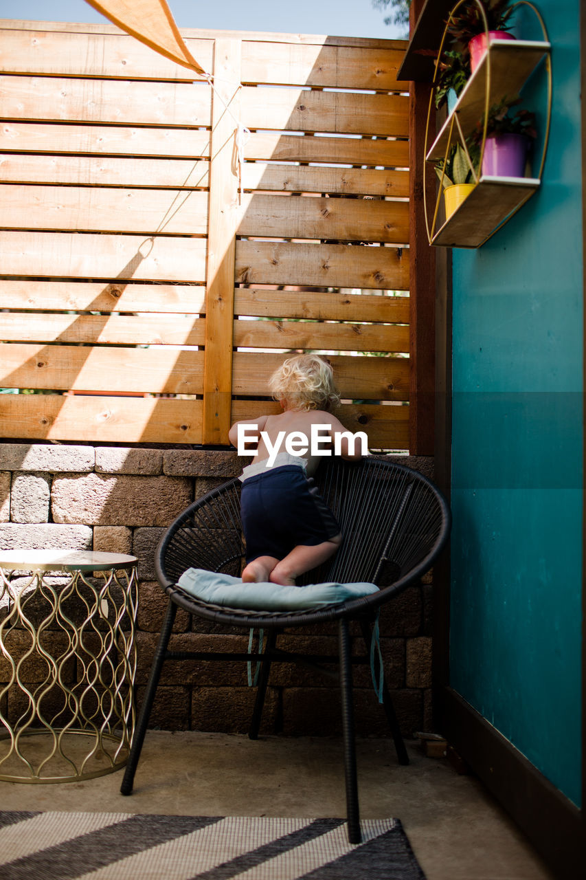 Two year old standing on chair while peeking through fence