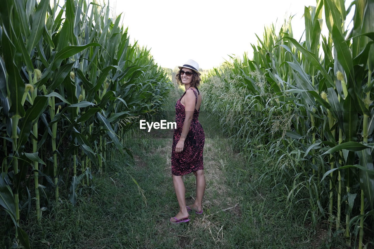 Portrait of smiling woman standing on field amidst cereal plants