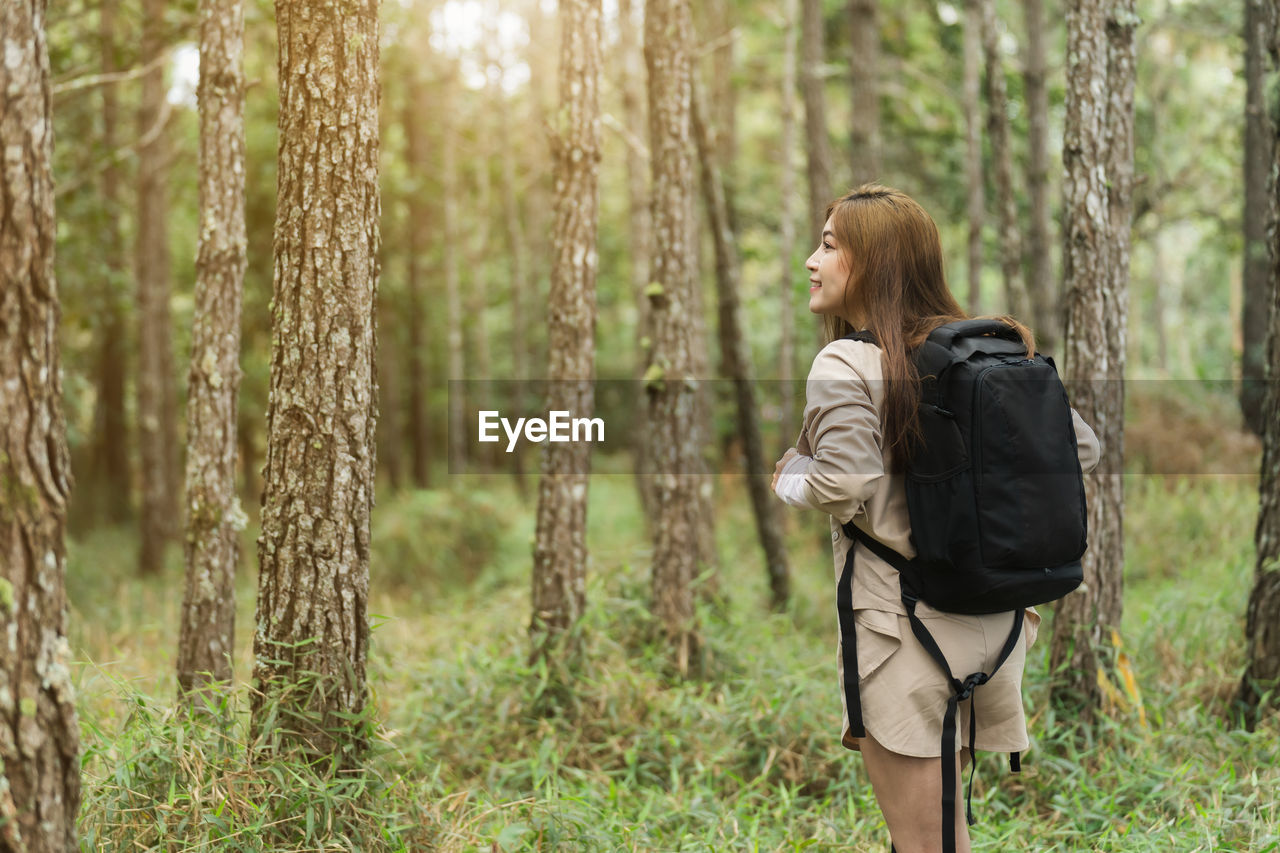 forest, land, one person, tree, plant, nature, women, natural environment, woodland, leisure activity, adult, lifestyles, young adult, clothing, backpack, hiking, autumn, exploration, grass, casual clothing, hairstyle, standing, outdoors, non-urban scene, day, three quarter length, trip, vacation, beauty in nature, tranquility, long hair, holiday, rear view, adventure, looking, person, female, landscape, walking, environment, travel, solitude, sunlight, tranquil scene, activity, meadow, focus on foreground, tourism, full length, emotion, tree trunk, wilderness, spring