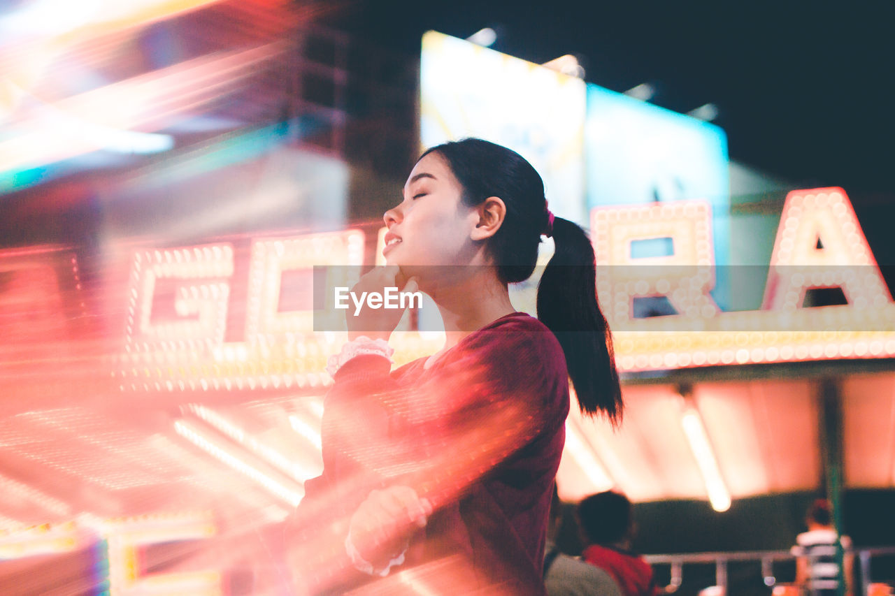 Low angle view of young woman in illuminated street at night