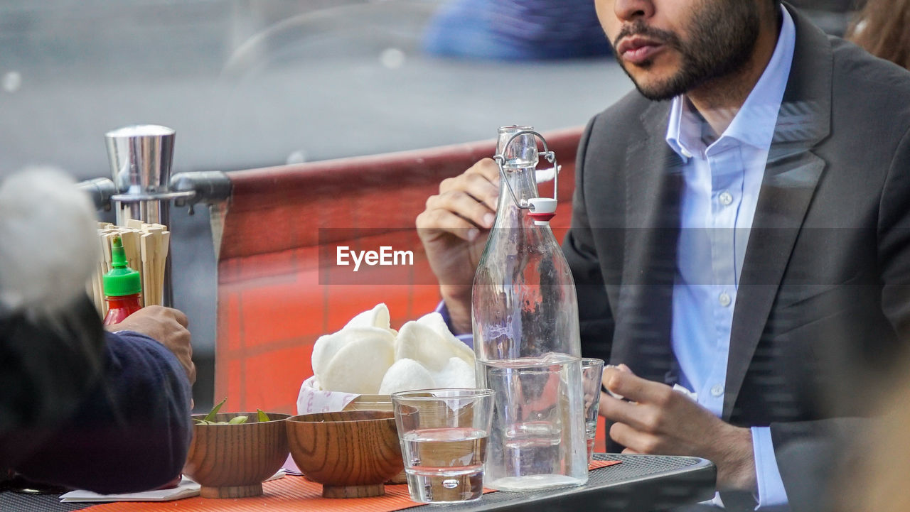 MIDSECTION OF MAN DRINKING GLASS ON TABLE AT CAFE