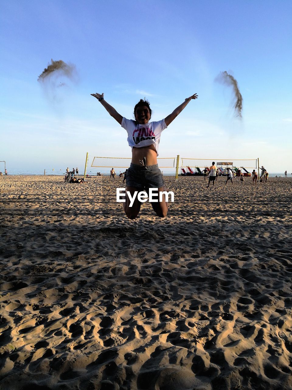 Happy woman throwing sand while jumping at beach