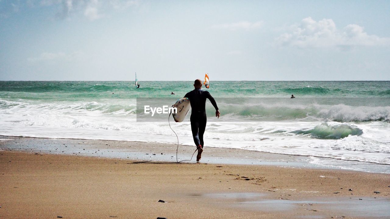 Full length of man with surfboard walking at beach against sky