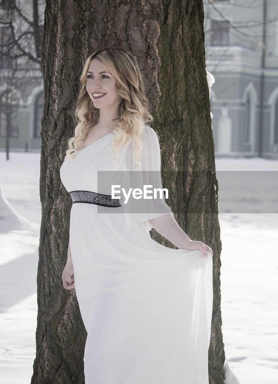 Smiling young woman looking away while standing on snow covered field