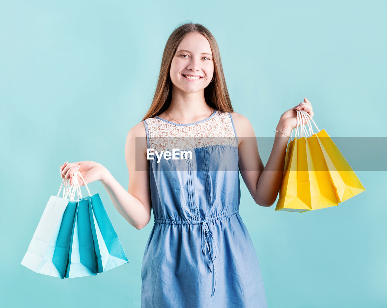 Shopping woman smiling. female teenager holding paper shopping bags isolated on blue background